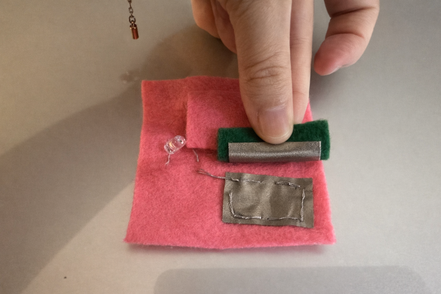 I created a switch in the bottom right corner. Under the felt is conductive fabric, and two pieces of conductive fabric touch each other. The pink area on top is the battery.