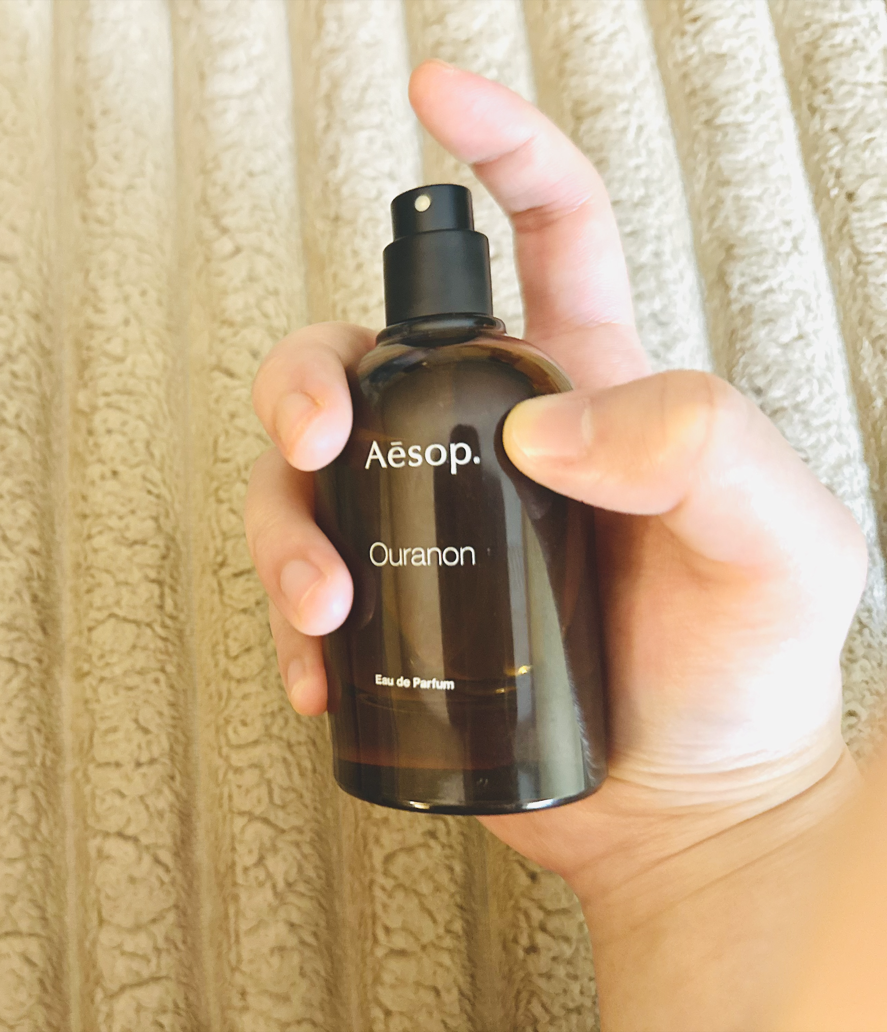 My hand holding the perfume bottle with my finger resting on the spray nozzle before pressing